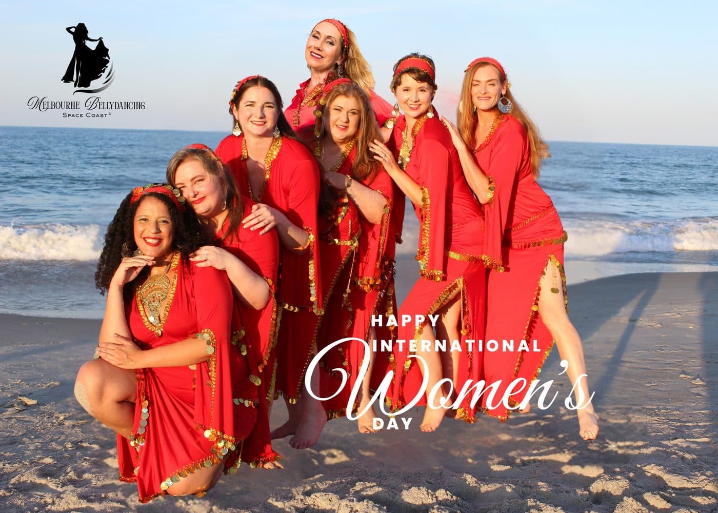 The troupe in red dresses on the beach for International Women's Day